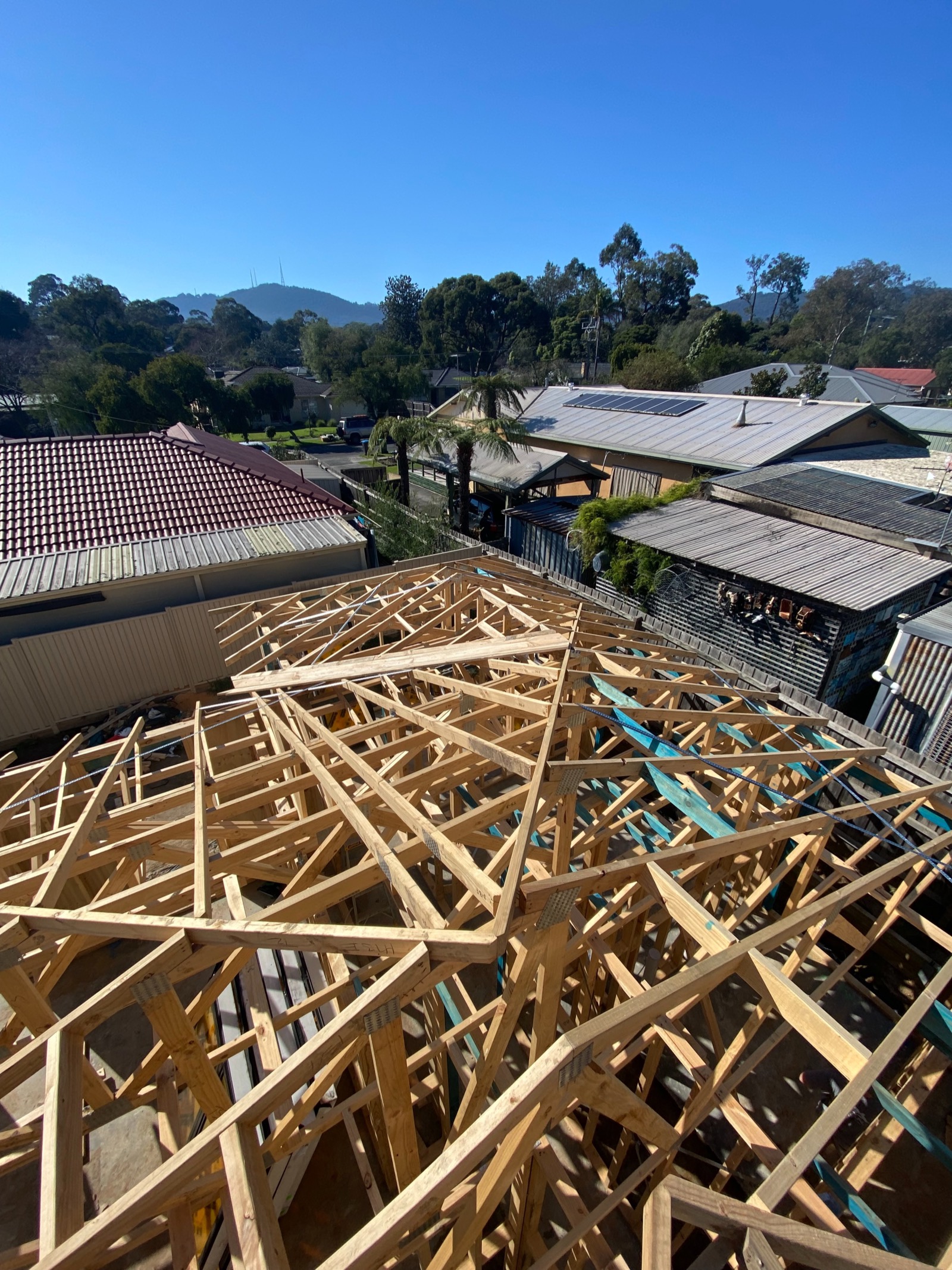 Roof trusses over a backyard single-storey frame in The Basin, with the Dandenongs behind